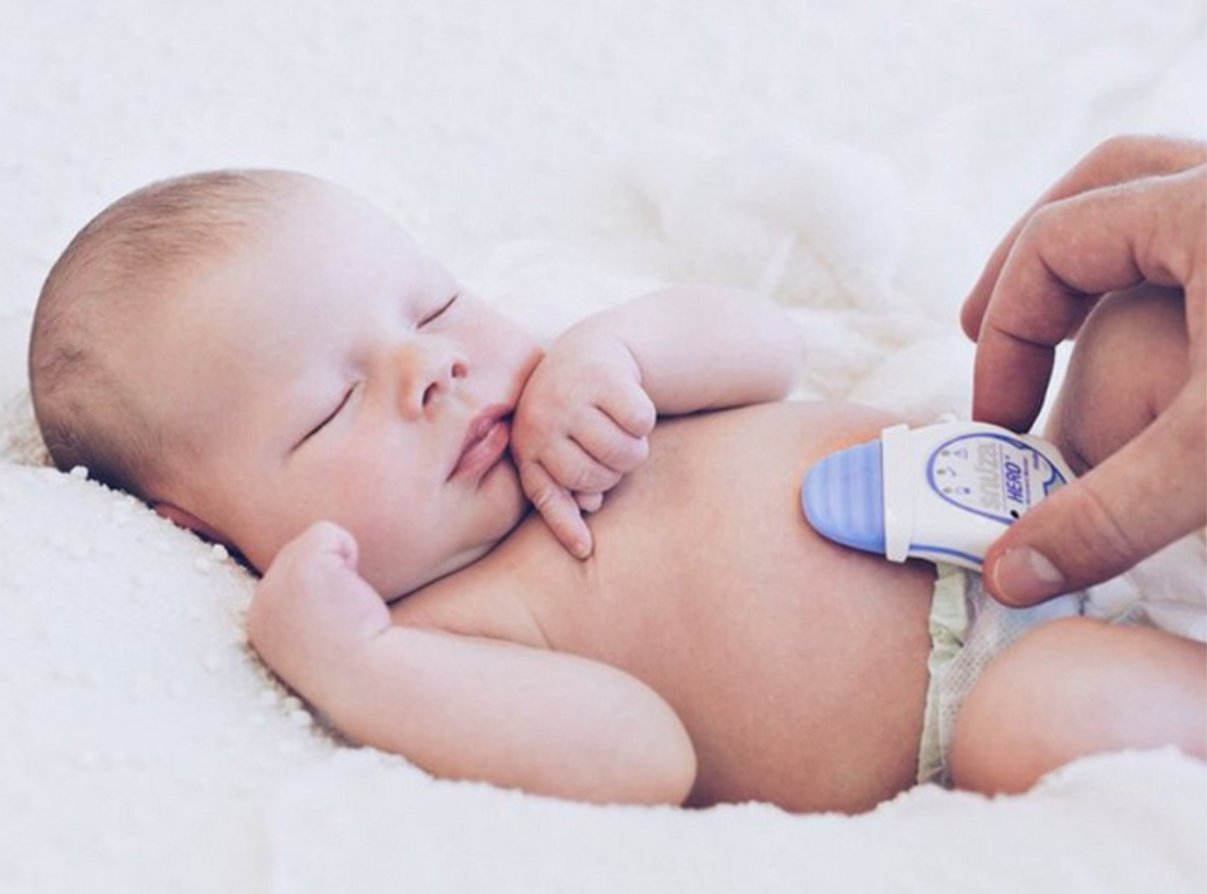 A sleeping newborn with a portable Snuza Hero MD breathing monitor clipped to the nappy